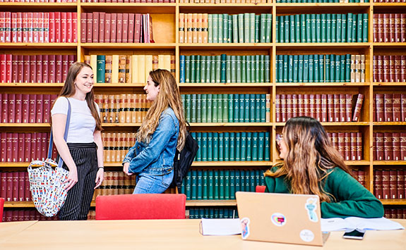 Students in the Law Library chatting next to bookshelves